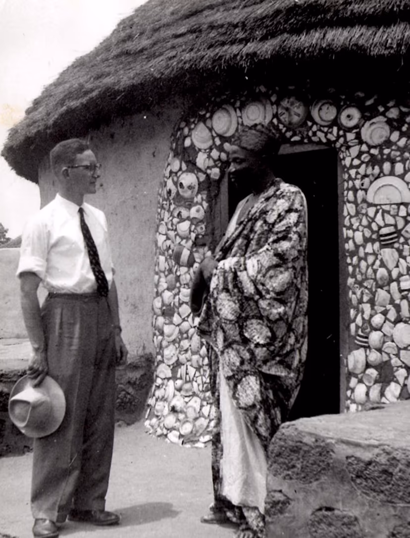 Alhaji Yakubu Tali, the Tolon Na, in a patterned smock outside a thatched compound, standing with a European official